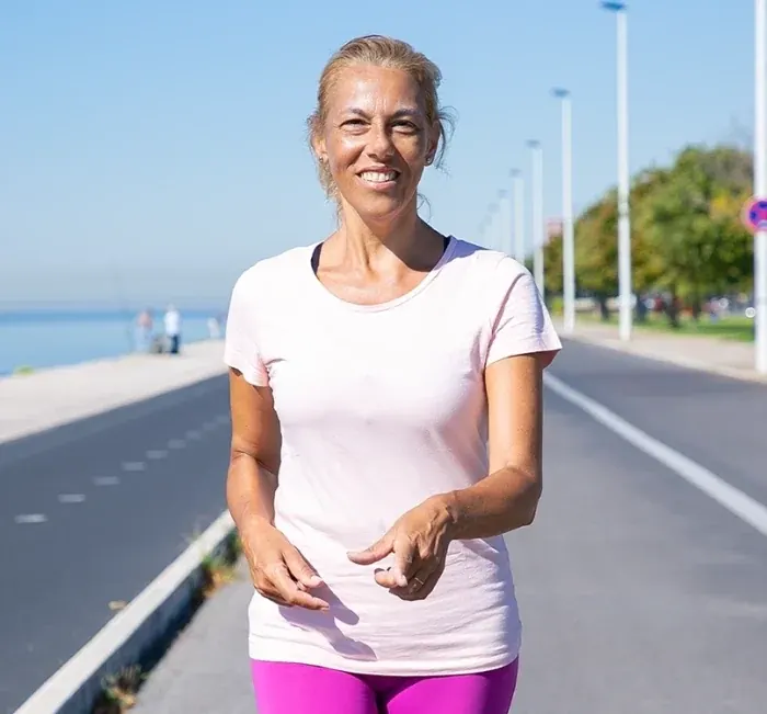 A smiling woman in a pink T-shirt walking along a seaside promenade