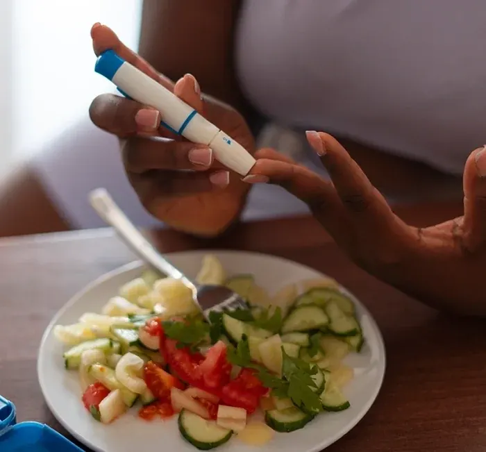 A person using a lancet pen to check blood sugar beside a plate of salad