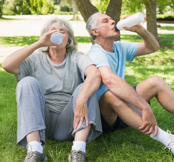 An older couple resting on the grass in a park, drinking water after exercise