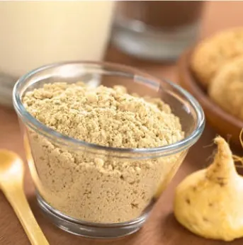 Pale maca powder in a glass bowl next to whole maca roots